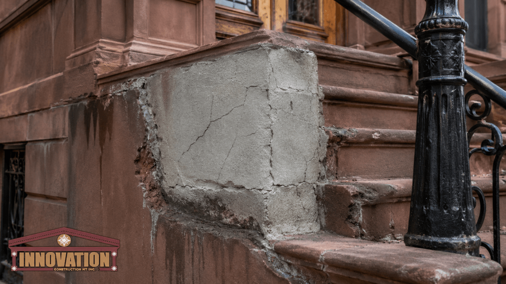 Close-up of a historic brownstone stoop with a cracked concrete patch, damaged stone edges, and ornate iron railing, highlighting improper repair on brownstone, with Innovation Construction NY logo.