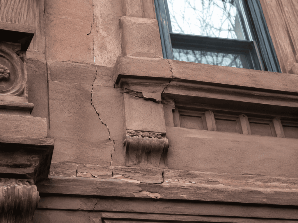 Brownstone Facade Repair on cracked NYC brownstone facade with damaged window surround and decorative stone details